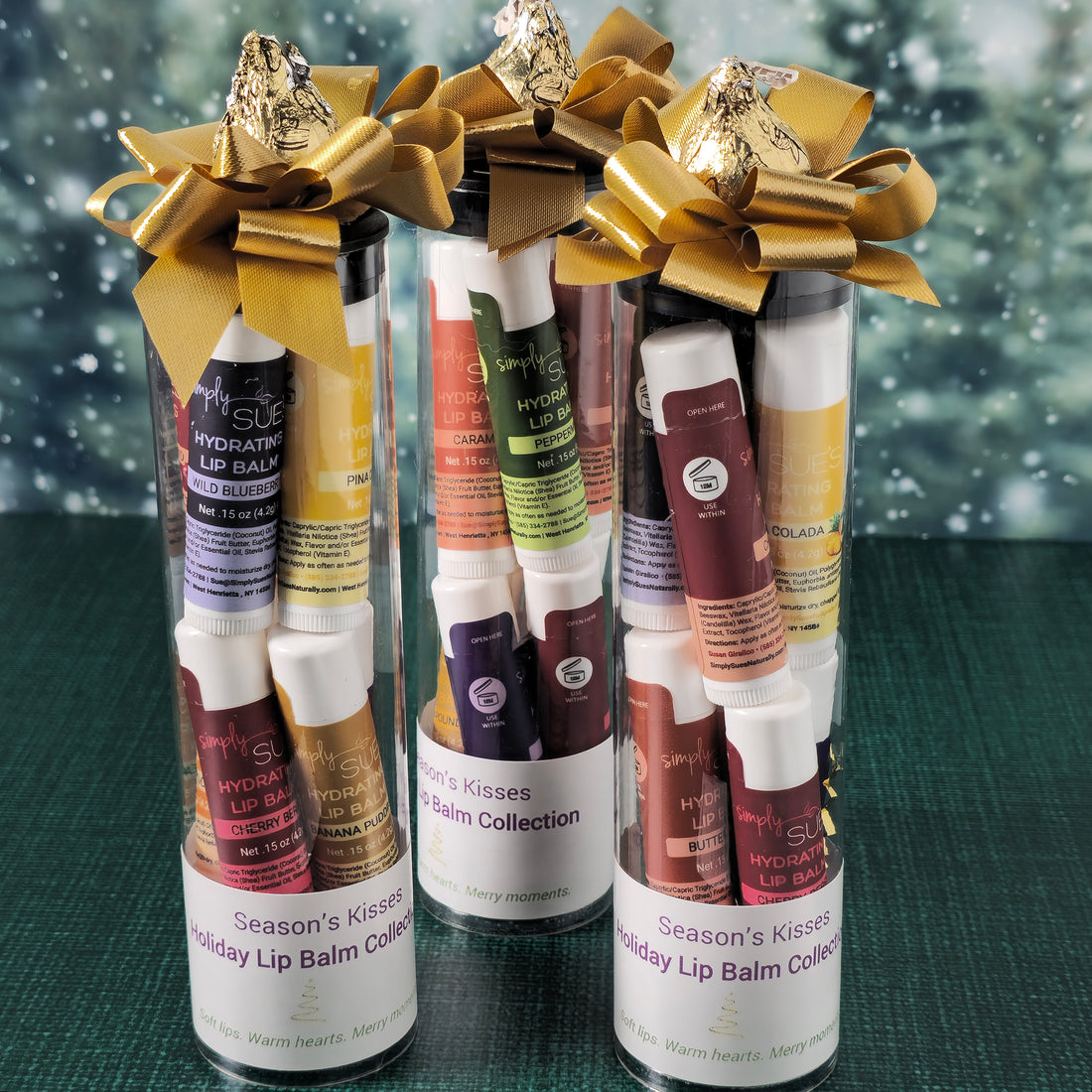 Three lip balm collections with gold bows against a snowy background