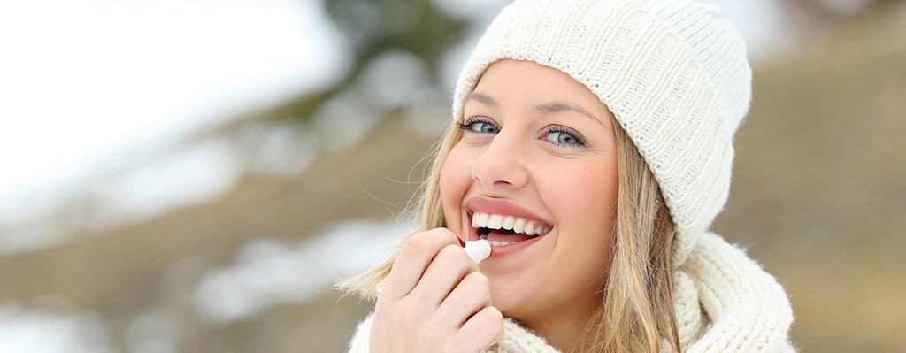 Smiling Mature woman outdoors wearing a winter hat applying natural lip balm