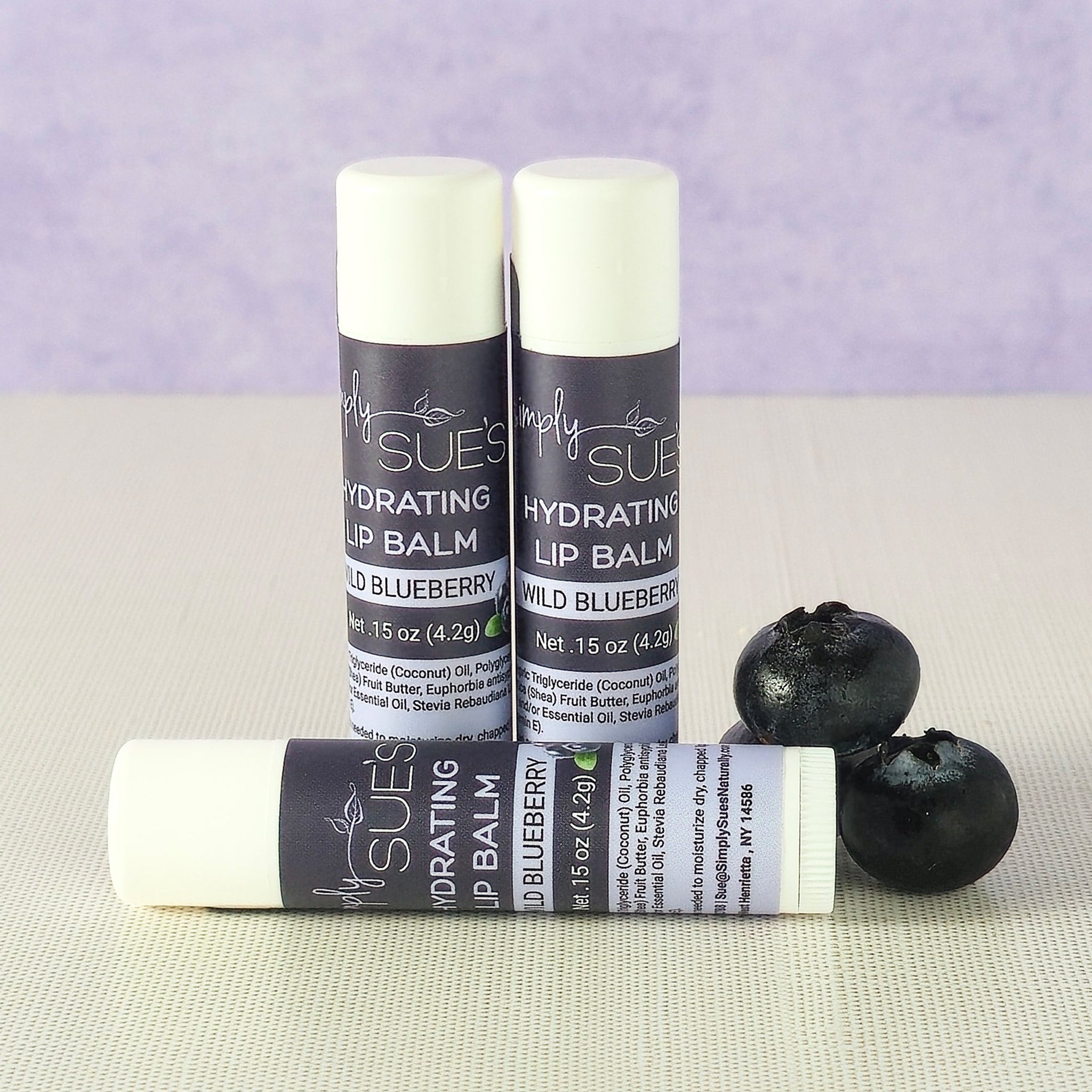 Wild blueberry lip balm tubes by Simply Sue’s with blueberries on a neutral background