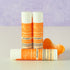 Creamsicle lip balm tubes by Simply Sue’s with orange slices on a neutral background