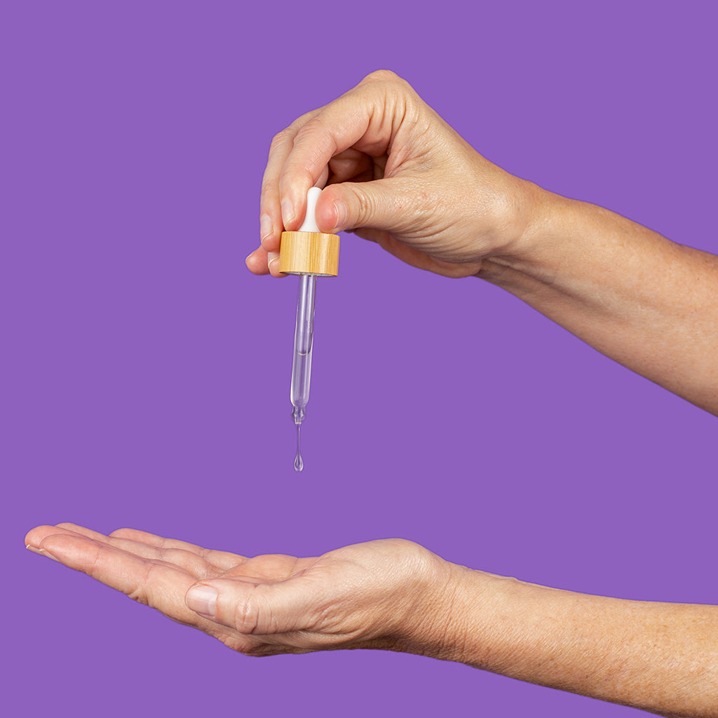A woman holding the dropper of Simply Sue's Facial Serum and applying a drop to her hand.
