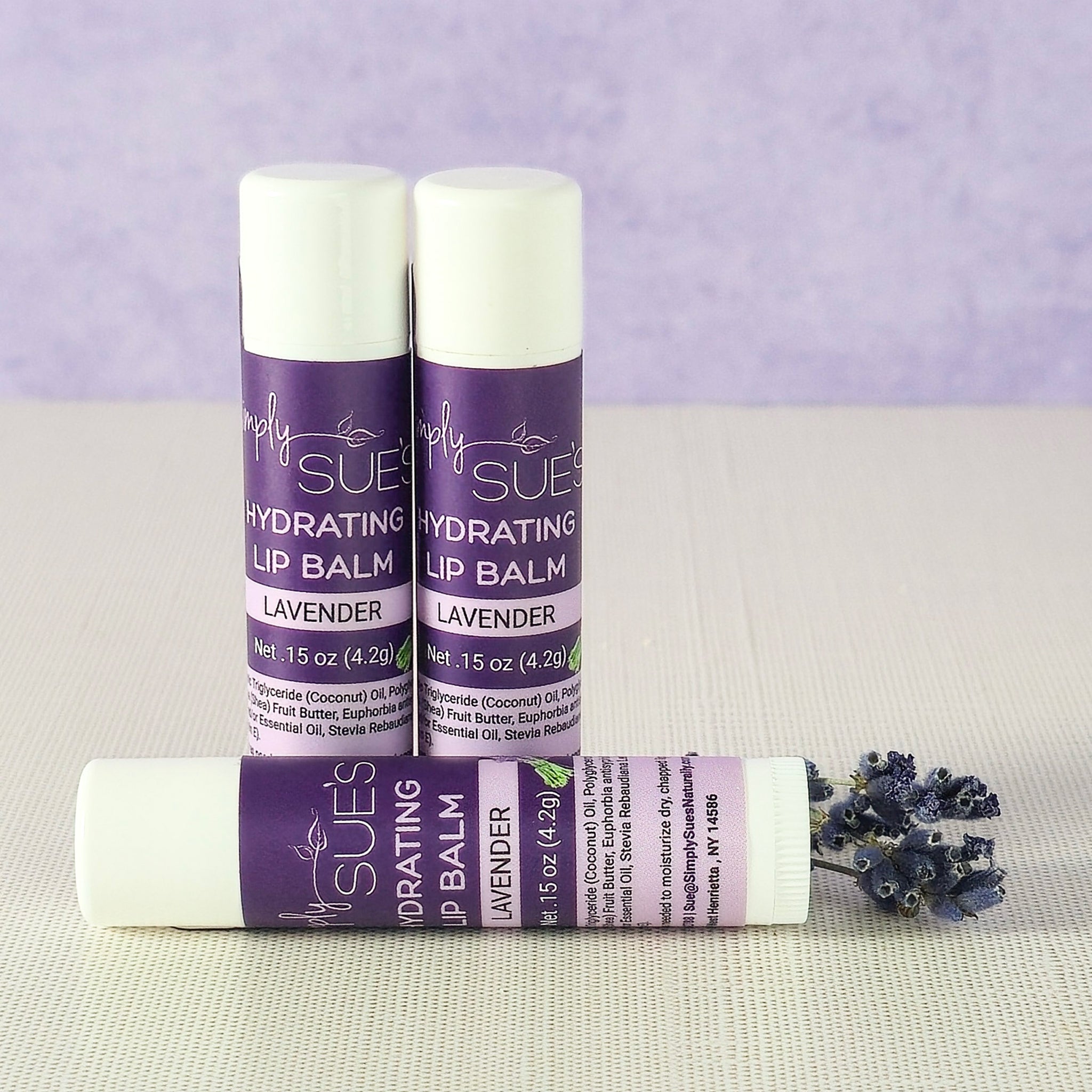 Lavender lip balm tubes by Simply Sue’s with dried lavender on a neutral background