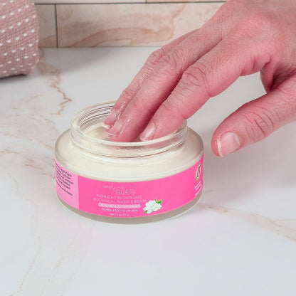 Hand applying cream from a jar with a pink label on a marble surface