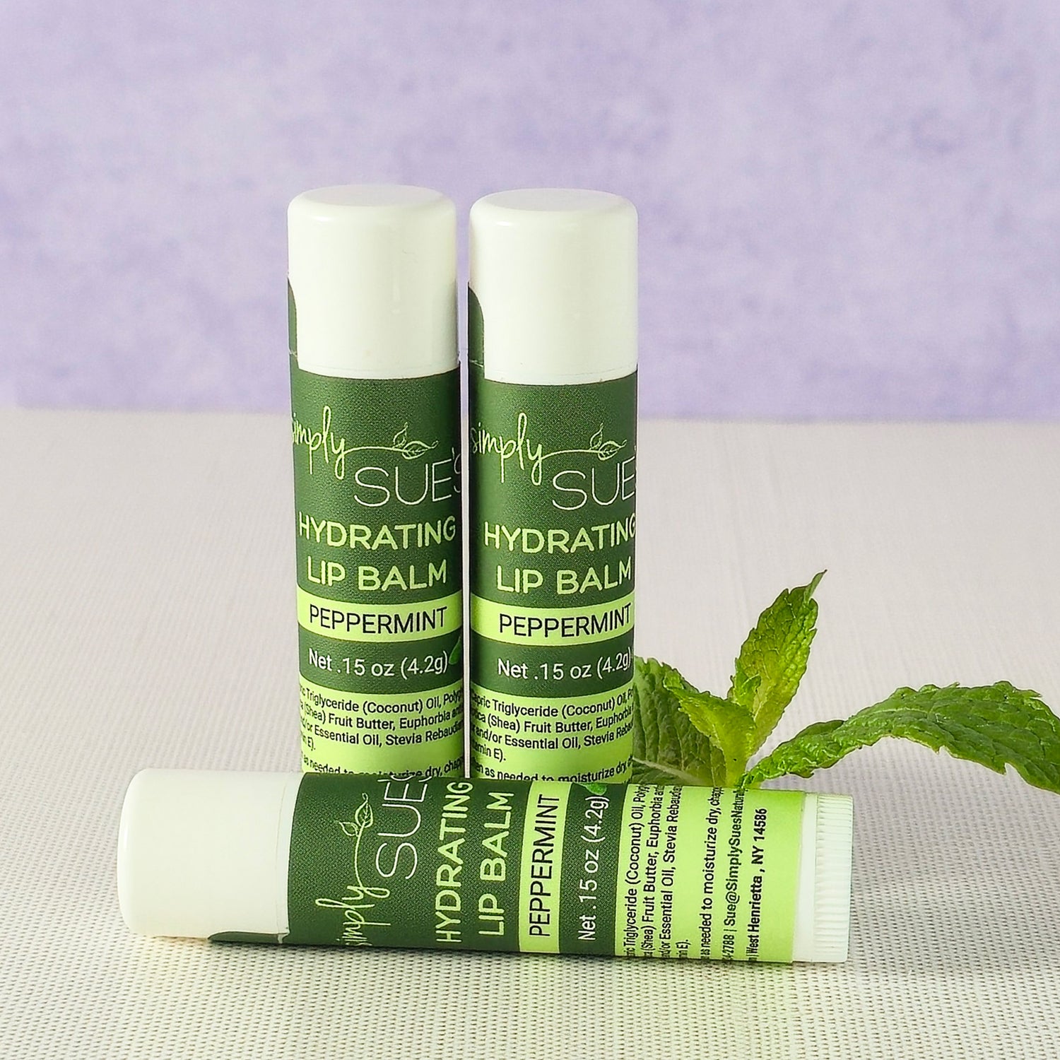 Peppermint lip balm tubes by Simply Sue’s with fresh mint leaves on a neutral background