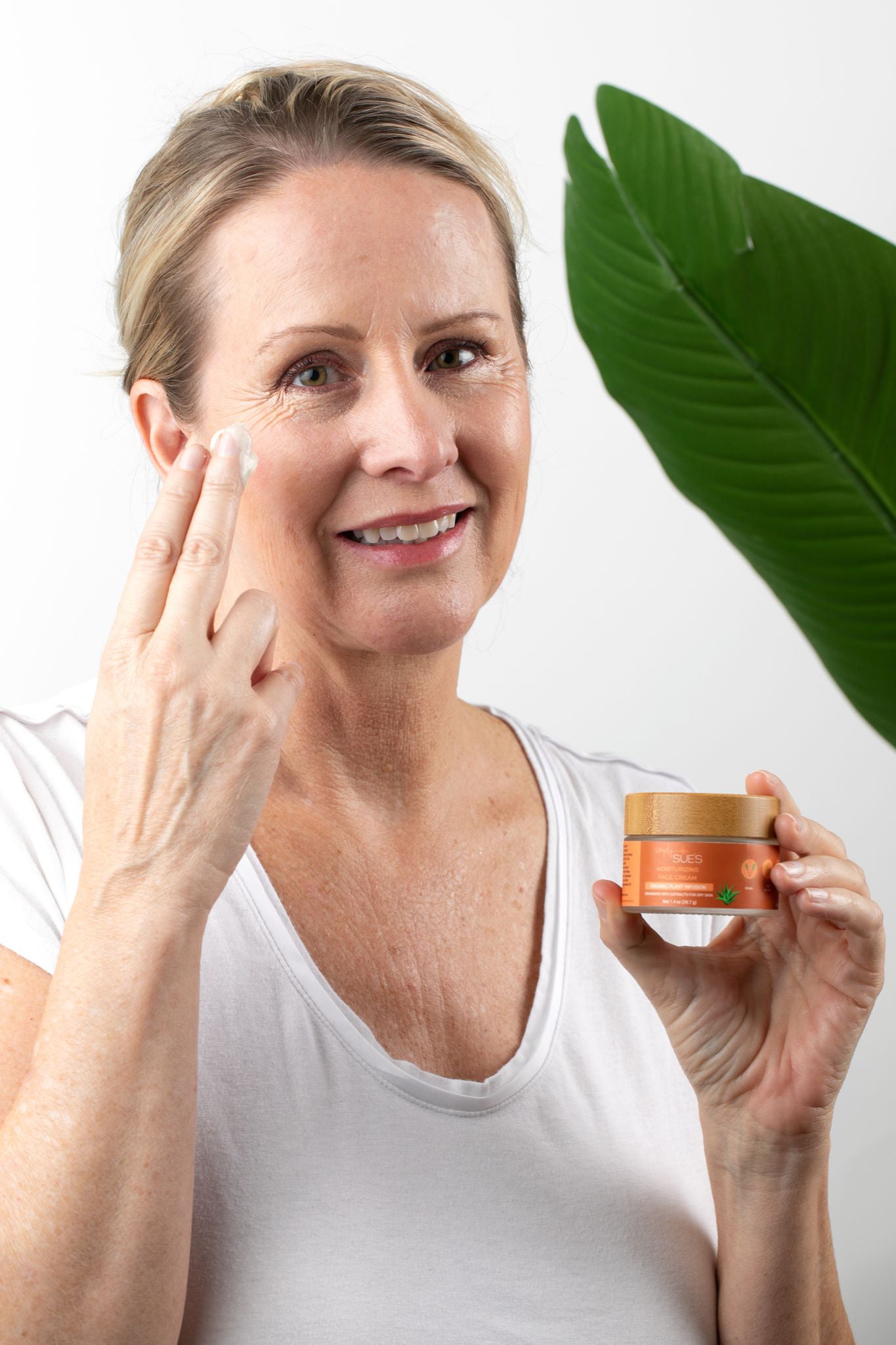 Woman holding jar of Moisturizing Face Cream and apply a small amount of cream to her face.