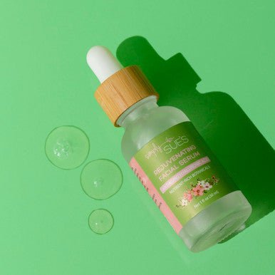 Rejuvenating Facial Serum in a glass bottle and bamboo dropper on a green background with serum swatches showing the texture.